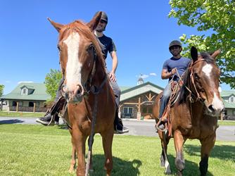 two horses and riders in front of a farm